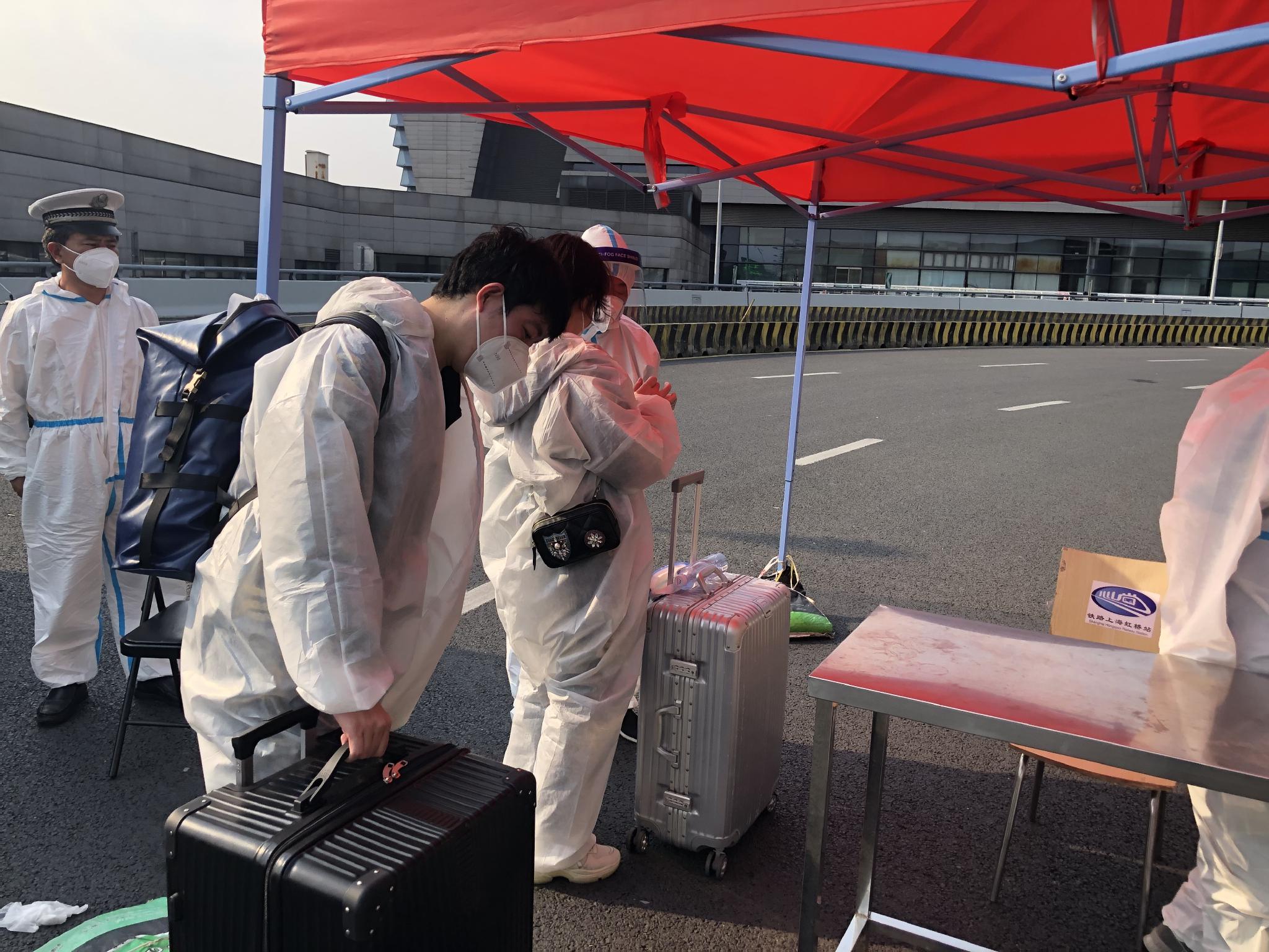 旅客提着行李箱走进虹桥火车站,站外查验当日车票、48小时内核酸阴性报告,进站前查验抗原检测报告。