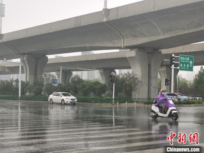 图为7月15日，郑州市区降雨，市民着雨衣出行。刘鹏 摄