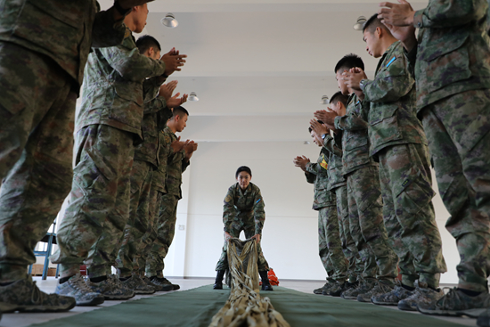 近日,空降兵某部文职教员赵莉(中)组织阻力伞折叠授课,为学兵示范折叠方法。臧猛/摄