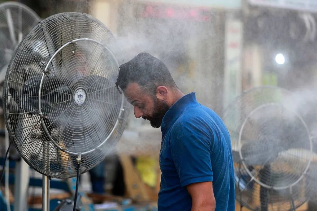 當地時間2023年7月23日，伊拉克巴格達，氣溫飆升，一名男子在霧化器前淋水解暑。視覺中國 資料圖
