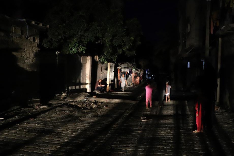 当地时间2023年10月16日，加沙地带的汗尤尼斯，人们借助车灯的光亮行走。