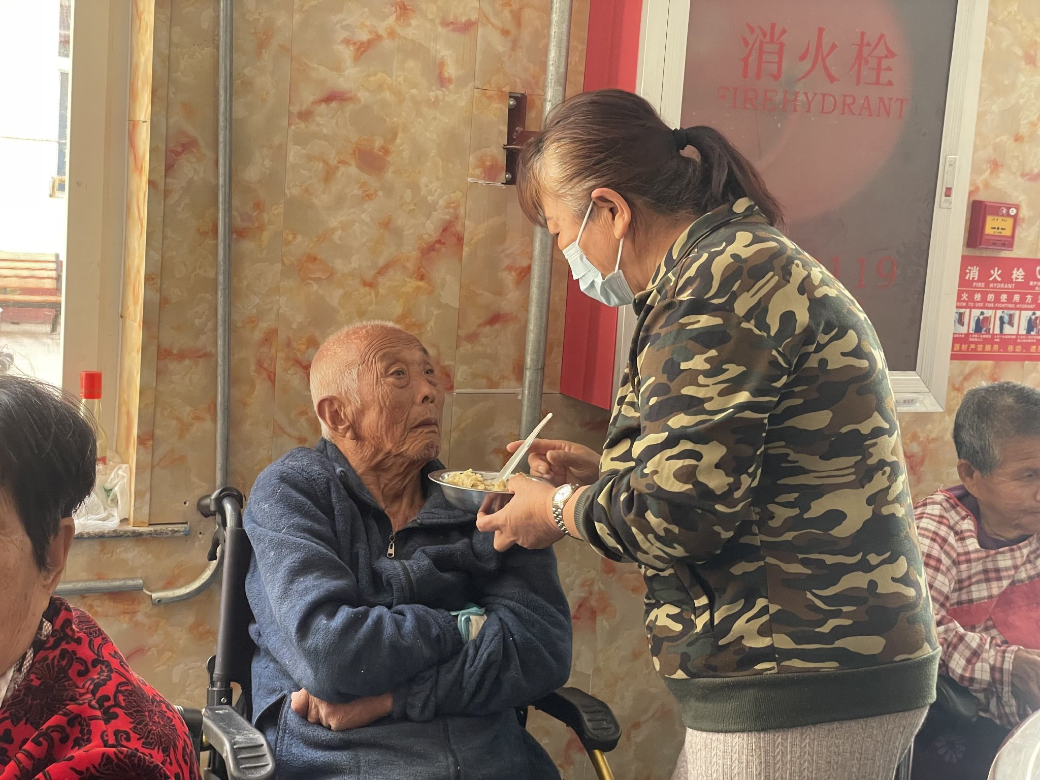李仲娥在給養老院里一位失能老人喂飯，她的兩鬢也有了花白的痕跡。新京報記者 趙利新 攝