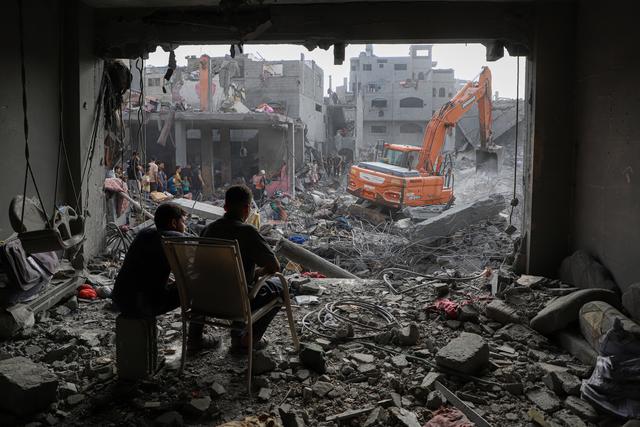 當地時間2023年10月25日，加沙地帶南部城市汗尤尼斯，當地居民圍觀挖掘機在以色列空襲後的建築廢墟現場作業。 新華社 圖