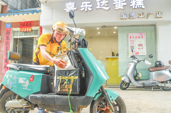 在海口一蛋糕店门口,美团骑手王健宇准备将外卖商品送到顾客手中。记者 孙士杰 摄