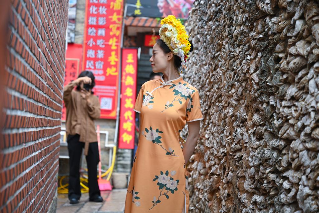 體驗“簪花圍”的遊客在泉州市蟳埔村的蚵殼厝旁拍照。新華社記者 周義 攝
