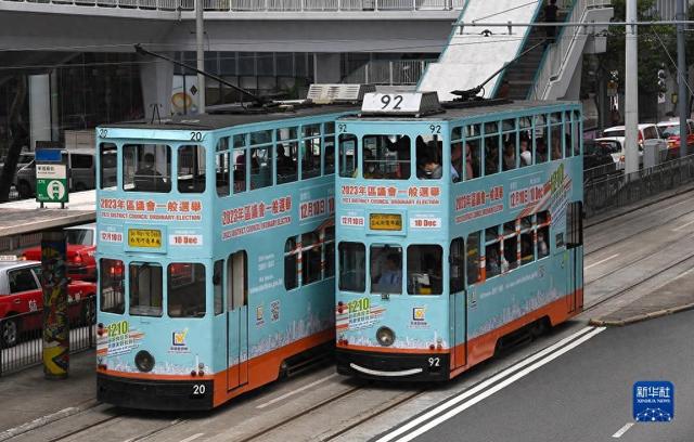 12月1日,两辆涂有2023年区议会一般选举宣传广告的电车从香港街头驶过。新华社记者 陈铎 摄