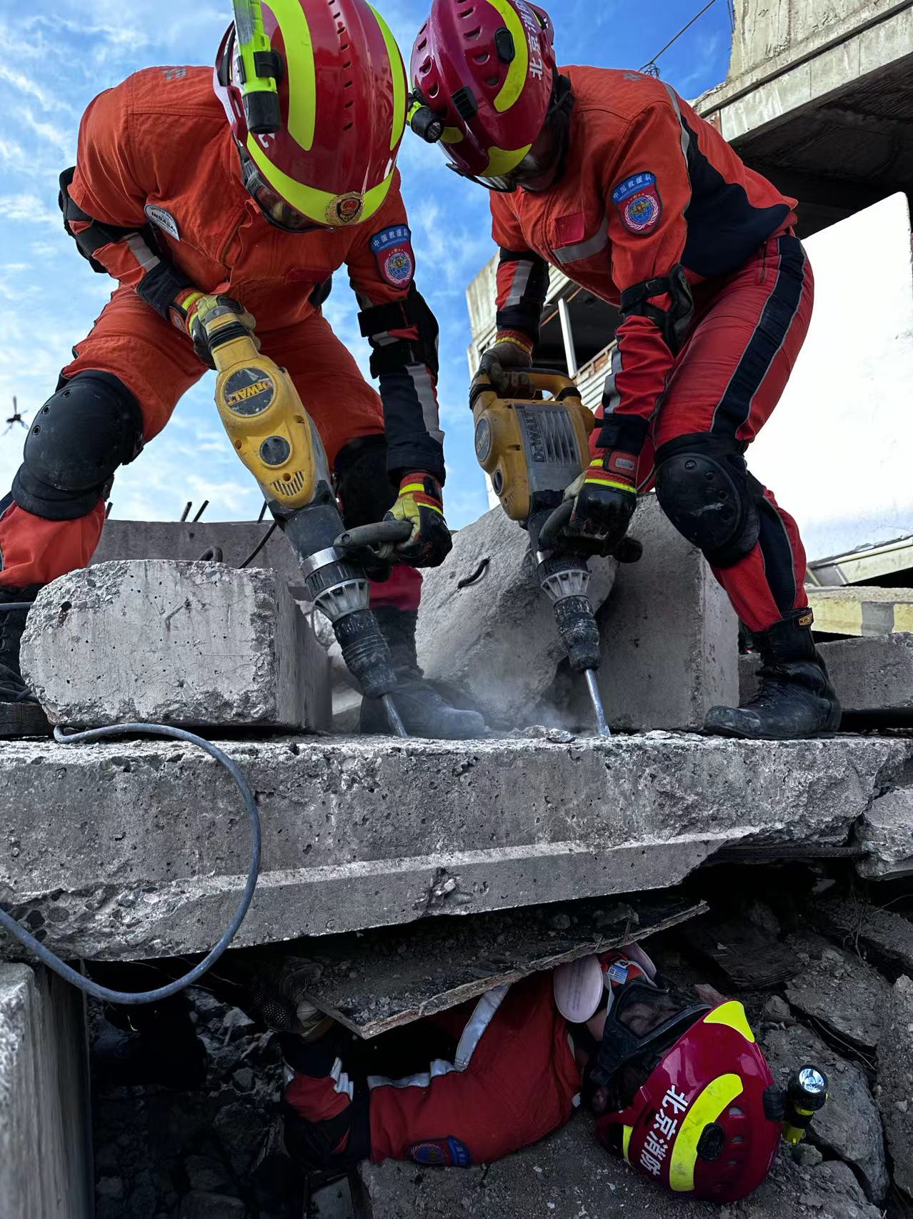 模擬地震救援演練中，兩個隊員在用鑿岩機鑿混凝土，下方隊員用木板接住掉下來的瓦礫，為被困者做遮擋。 受訪者供圖