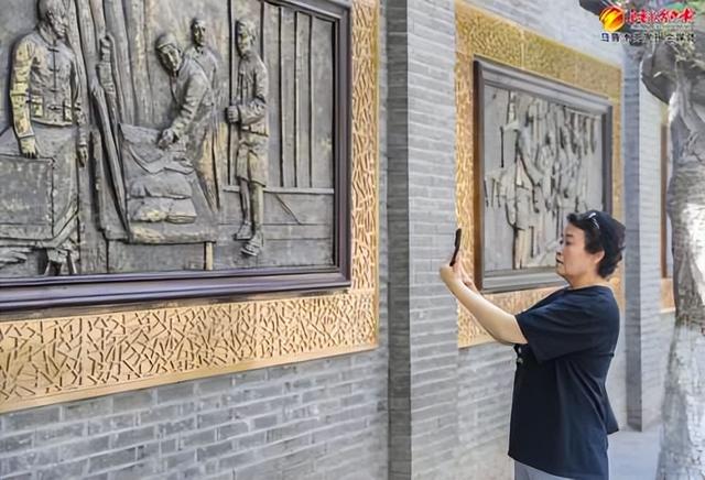 8月13日,在位于天山区的明德路,行人王丽用手机拍摄“工夫市”主题浮雕墙。 记者米热扎提·木塔力甫摄
