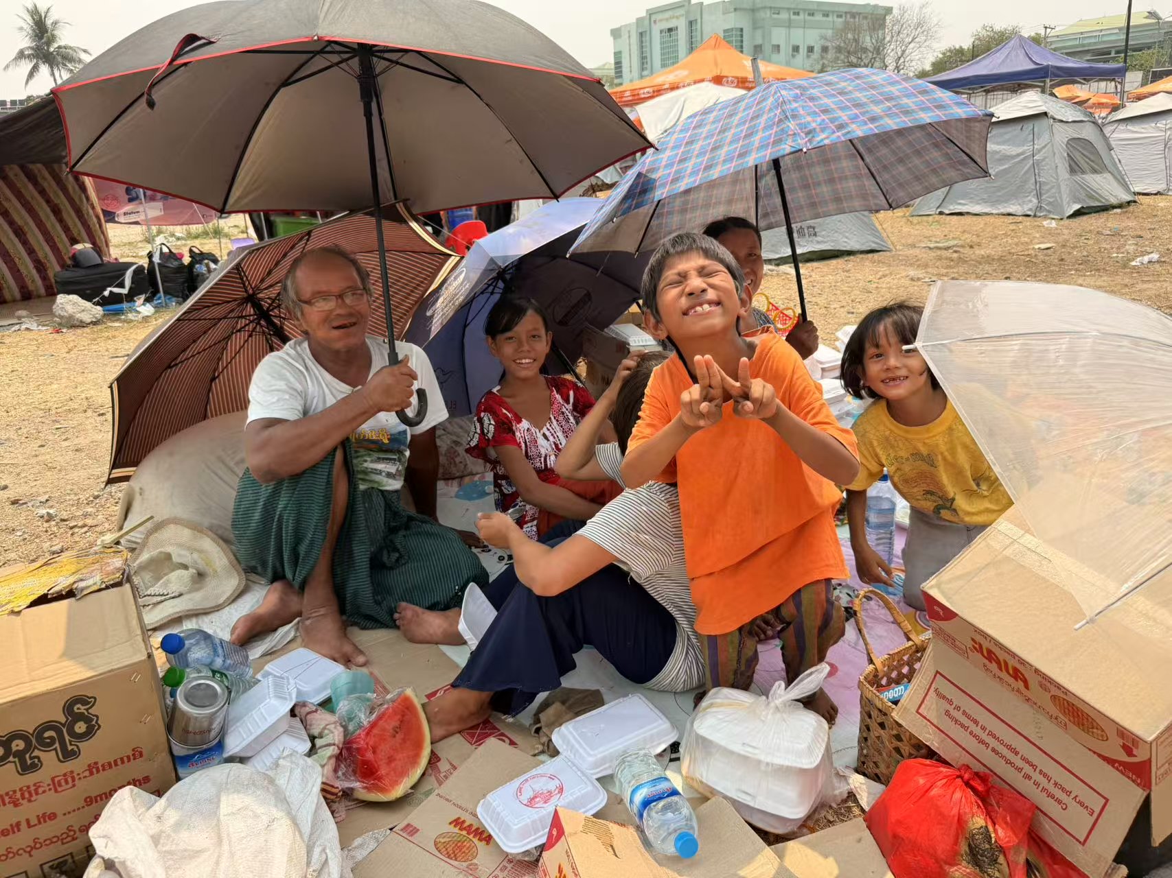 4月1日中午,曼德勒市最大的災民避難廣場上,一家人沒有帳篷,一同打傘遮陽。新京報記者 叢之翔 攝