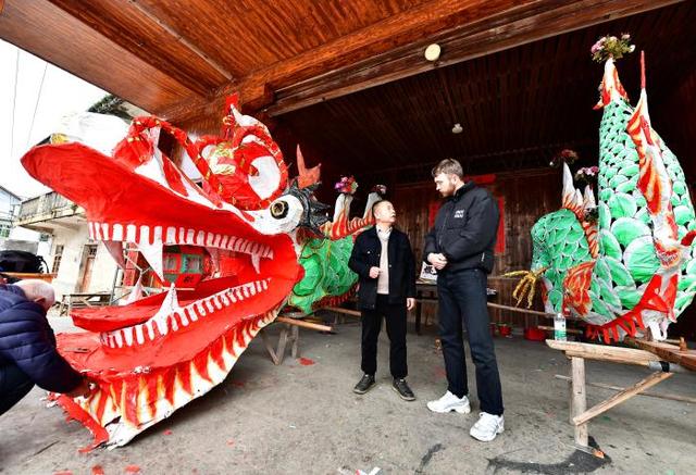 2025年2月11日,德国留学生王帅(右)向福建省龙岩市龙岗村村民了解当地闹元宵游大龙习俗。中新社记者 张斌 摄