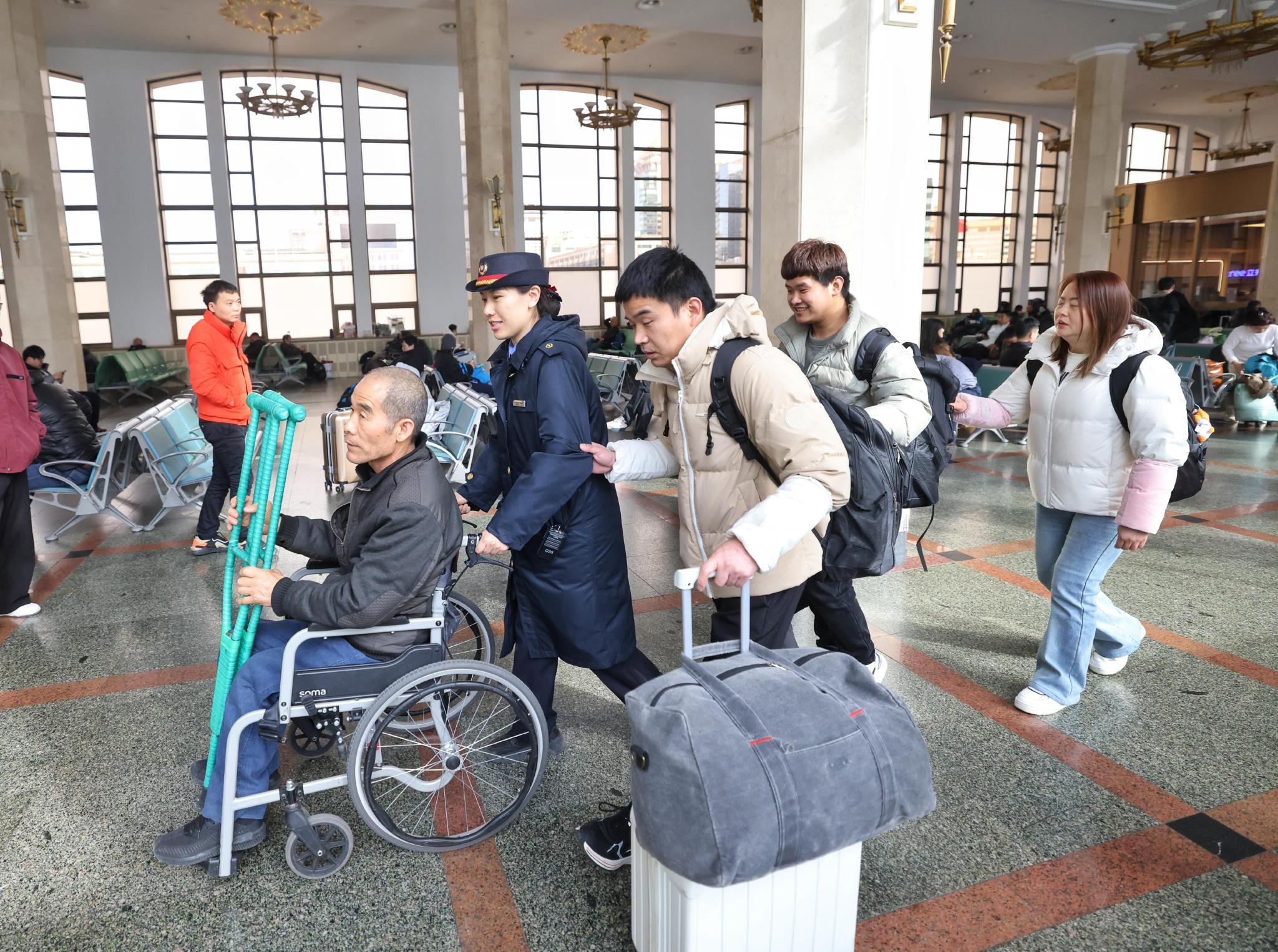 北京站京鐵愛心服務組客運員龔雪鈺身前推著一位行動不便的輪椅旅客，身後三位盲人旅客搭著她的肩膀前行。新京報記者 王貴彬 攝