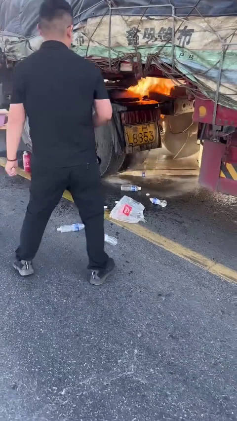 半挂车轮胎起火，路边男子提着矿泉水，面对翻倒的卡车，展现平凡英雄的一幕