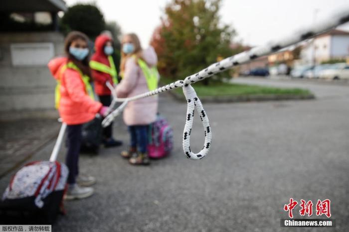 当地时间10月20日,在意大利北部贝卢斯科,孩子们拿着绳子保持社交距离,在志愿者的护送下走向学校。图为绳子上每隔一定距离就打一个结,帮助孩童确定距离。