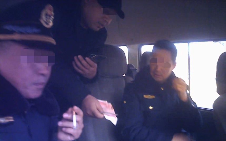  两名身着制服的交通执法人员，向超载货车司机收钱。视频截图