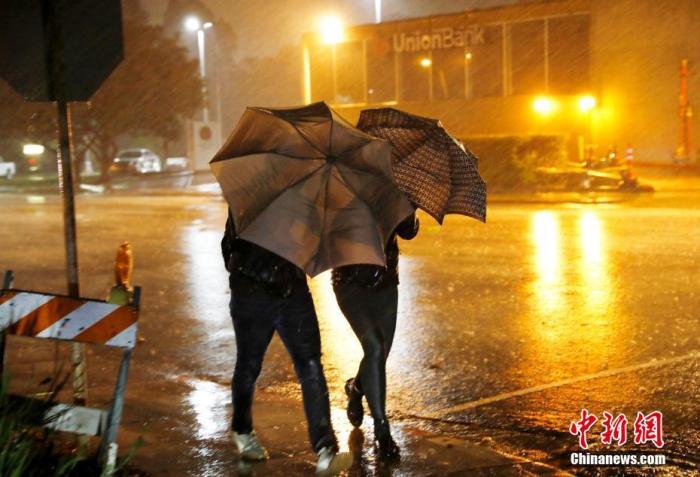 资料图:美国民众在狂风暴雨中前行。中新社记者 刘关关 摄