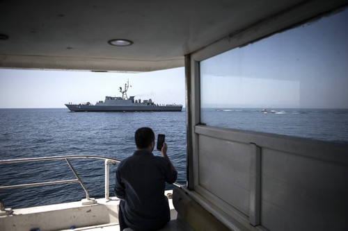 资料图片：2019年4月30日，一名男子用手机拍摄在霍尔木兹海峡巡逻的伊朗军舰。新华社发