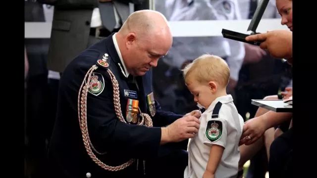 △在葬礼上，牺牲消防员年幼的儿子小哈维替父亲带上一枚沉甸甸的勋章