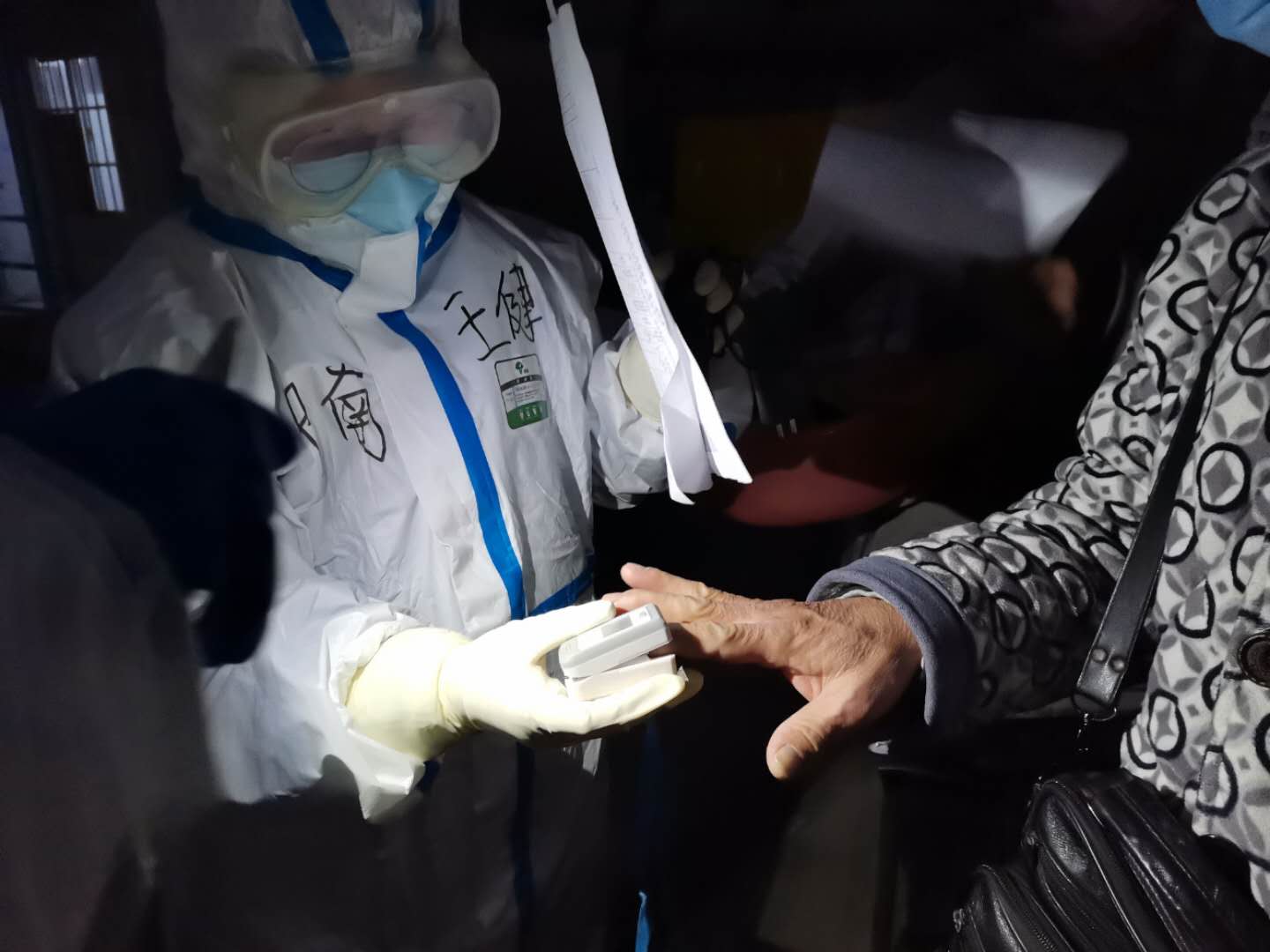 “方舱医院”外，身穿防护服的护士在检查病人的血氧饱和度