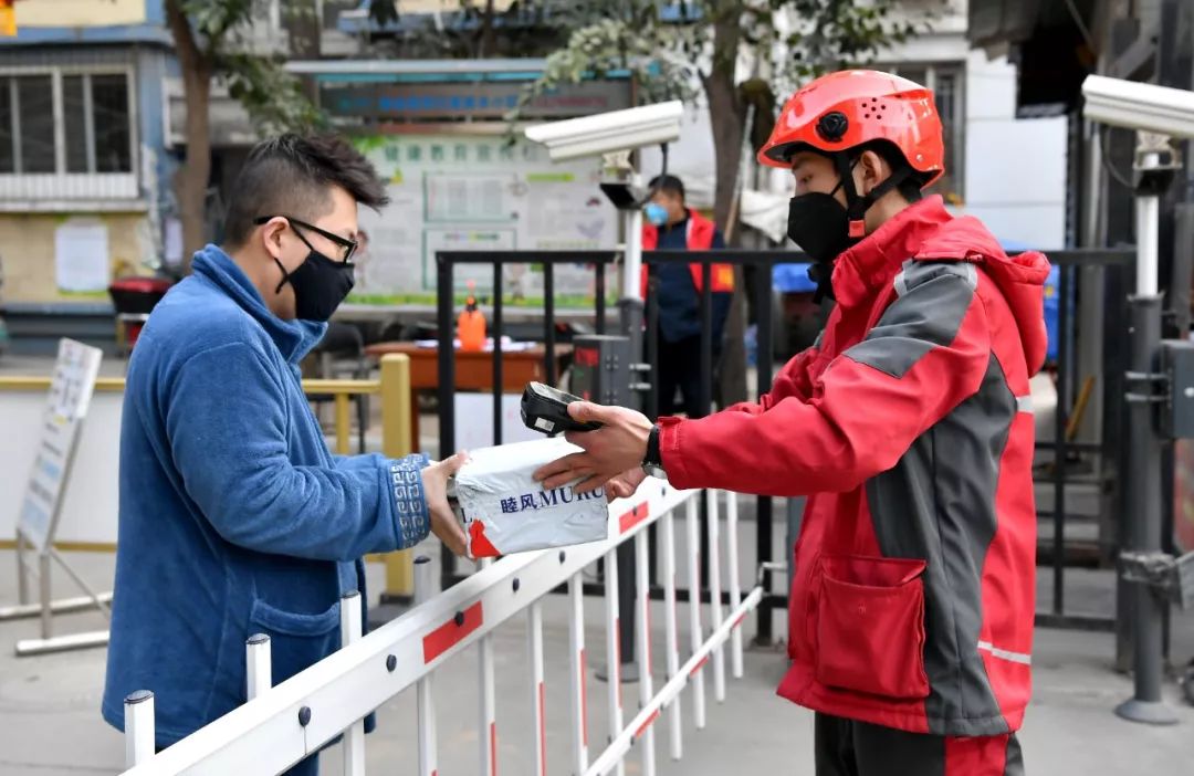 2月3日,西安一名快递员在一小区门口将货品交给收货人。新华社记者 刘潇 摄