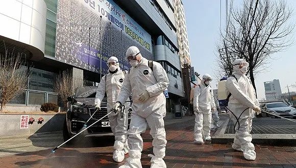韩国大邱市,工作人员正在消毒,其身后建筑张贴着新天地教会的宣传广告。图片来源:Yonhap