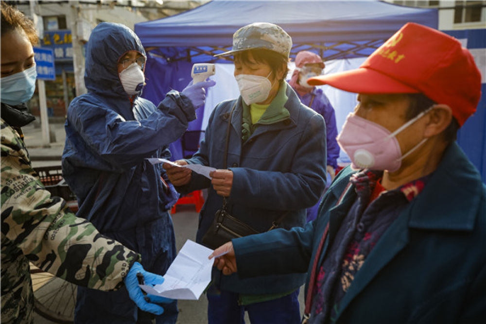 △2月22日，在武汉市百步亭社区建设新村，社区工作人员（左一、左二）在出入口查看居民进出凭证，并为居民测量体温