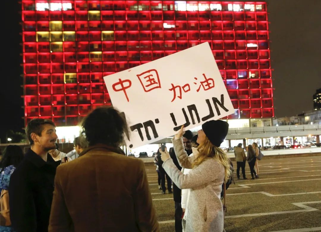 2月11日,在以色列特拉维夫市政大楼前,一名女子手举带有“中国加油”字样的宣传板,宣传板上用希伯来语写着“我们在一起”。新华社发(吉尔·科恩·马根摄)