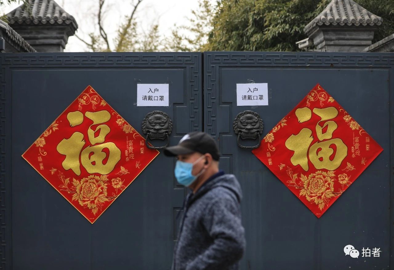  △2月27日，后海北沿，戴口罩的行人从贴有福字和“入户请戴口罩”的提示标语前经过。摄影/新京报记者浦峰
