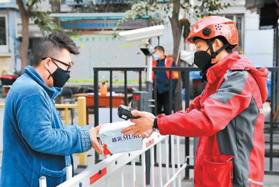 图为一名快递小哥（右）在一小区门口将货品交给收货人。 新华社记者 刘 潇摄