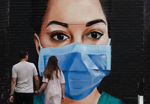 4月26日，在英国伦敦，一对情侣从一幅画有戴口罩医护人员的壁画前走过。新华社记者韩岩摄
