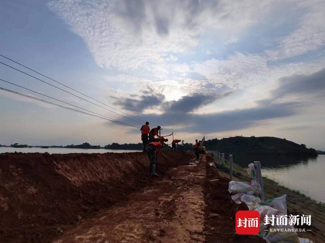 阻隔在洪水(左)与水库(右)之间的堤坝,被村民视为“第二道防线”。武警官兵正在帮忙增加沙袋,加固、增高堤坝。