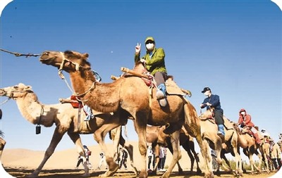 旅游市场有序开放，甘肃敦煌鸣沙山迎来一批批游客。图为游客骑着骆驼在沙漠中畅游。　　蒙钟德摄（人民图片）