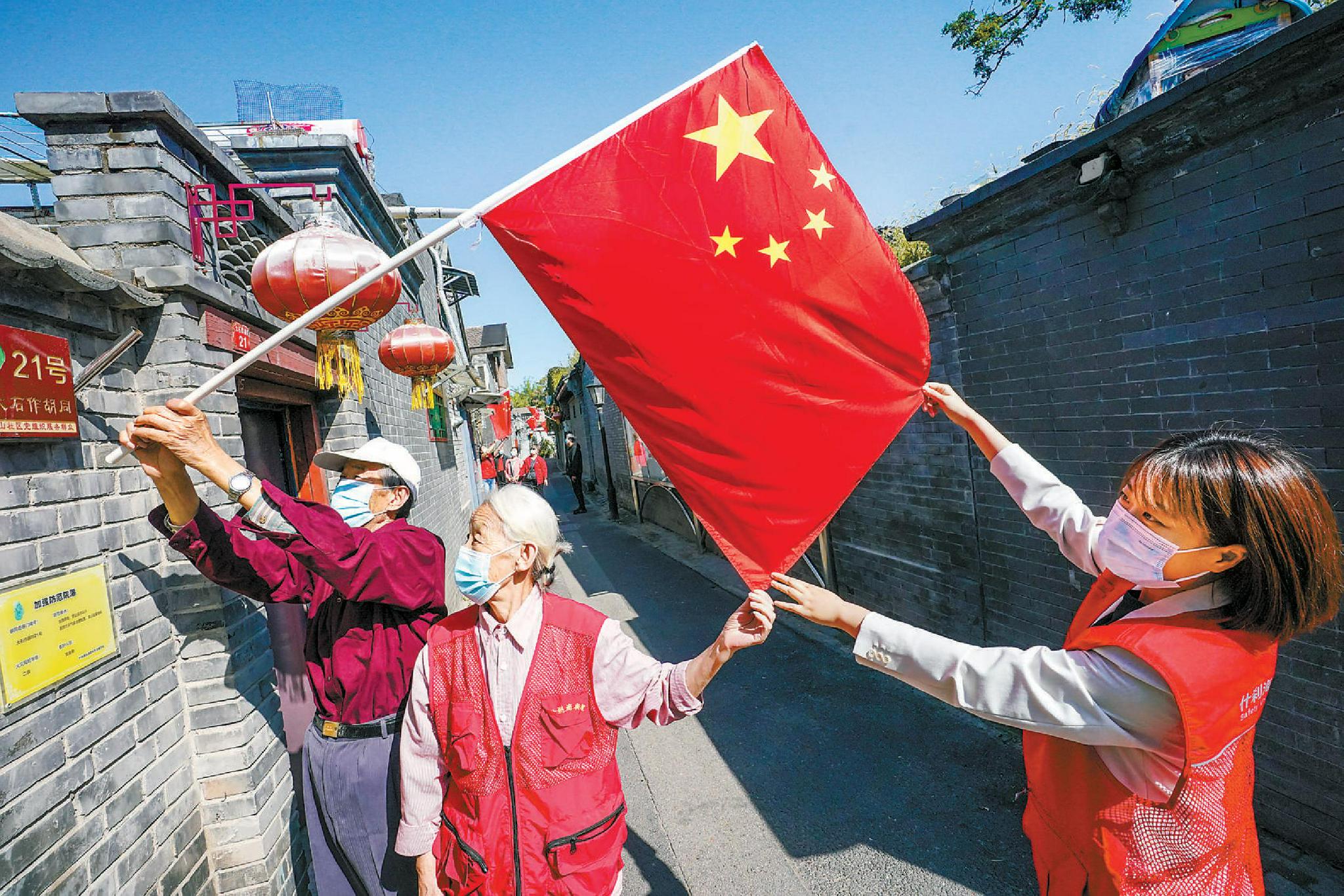 在什刹海街道大石作胡同，景山社区的社区工作者与居民们一同将鲜艳的五星红旗挂起，喜迎国庆。 方非 摄