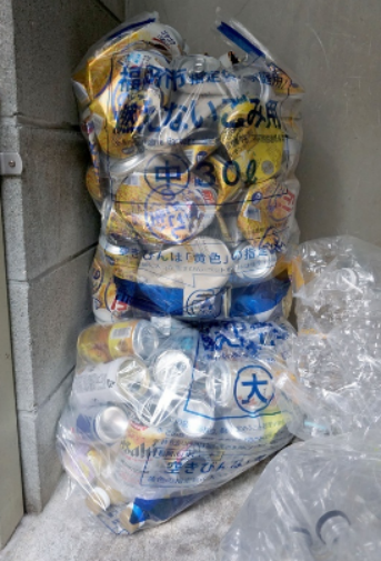 《西日本新闻》文章配图，装满易拉罐的垃圾袋