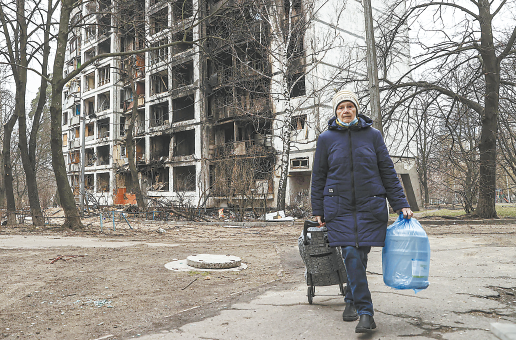 30日，在基辅街头，一名老人走过被炸毁的建筑物。