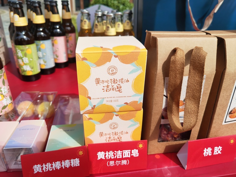 在现场展台上,黄桃汽水、黄桃橄榄油洁面皂、黄桃棒棒糖等新产品,造型包装青春有趣,充满活力。(束涵 摄)