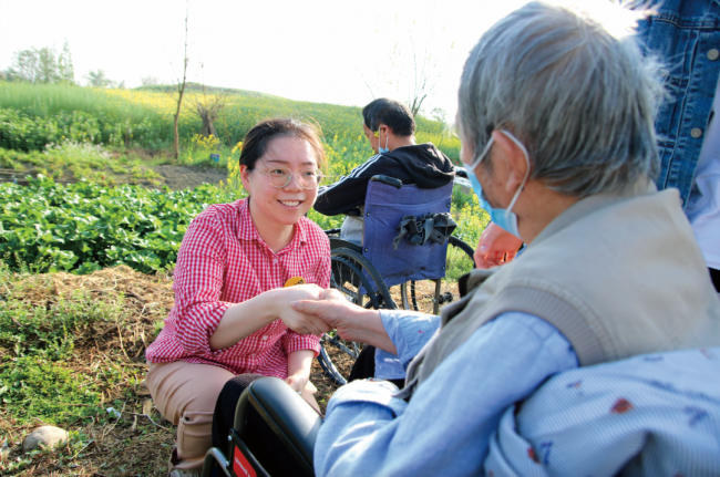 覃瑶琴正在和护理区居民赏油菜花田