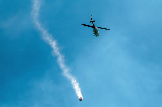 當地時間2023年6月5日，加拿大不列顛哥倫比亞省，阿爾伯尼港附近，一架直升機載著水桶灑水滅火。圖/視覺中國