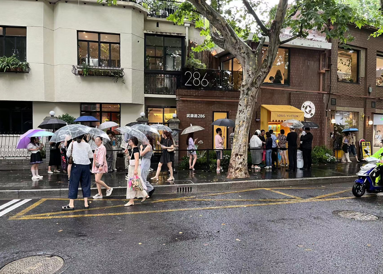 ↑门店外,人们在雨中排起了队