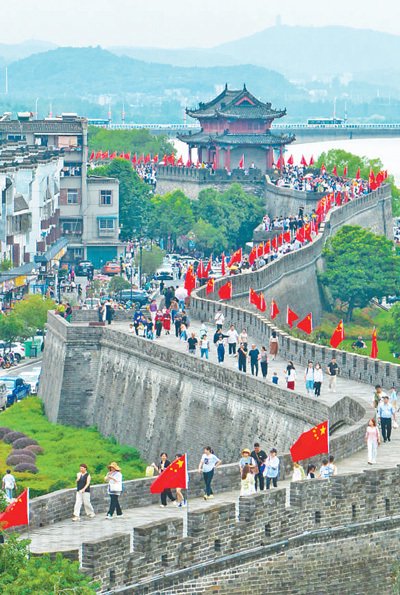 连日来,湖北省襄阳市街头、景区等地,五星红旗招展。图为9月30日,游客在襄阳古城景区游览。