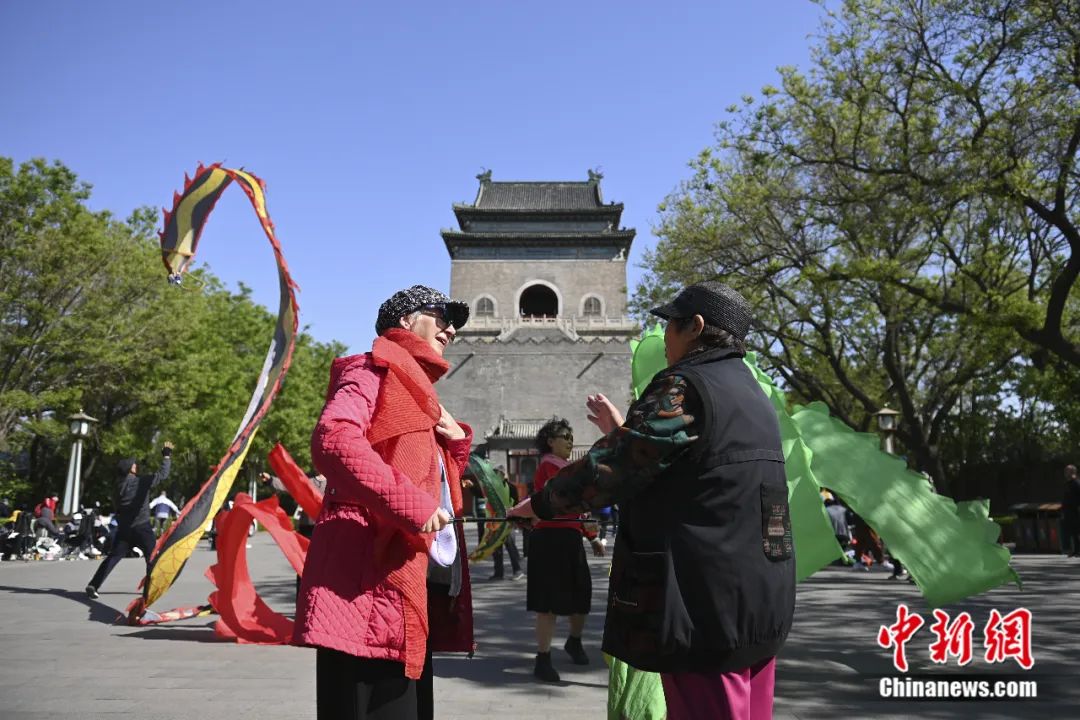 2023年4月26日,外国友人在钟鼓楼下与北京市民探讨舞动“彩带龙”的方法。田雨昊 摄