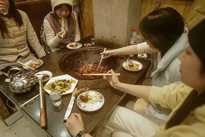 几名南方来哈尔滨旅游的姑娘一起尝试铁锅炖,这是一道具有代表性的东北菜式。