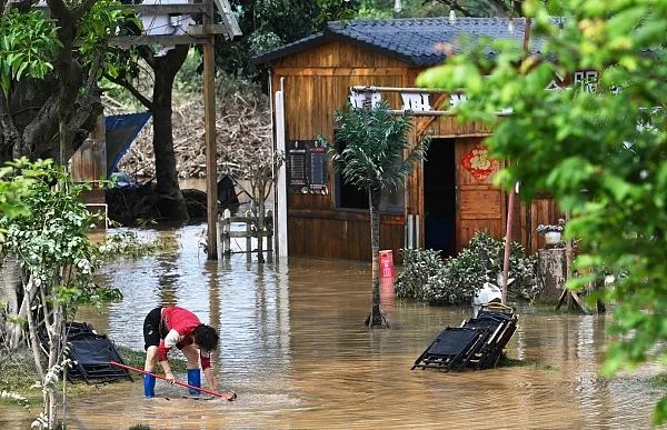 2024年4月24日，廣東清遠，暴雨過後，一名婦女在泥濘的水中撿椅子。（圖|視覺中國）