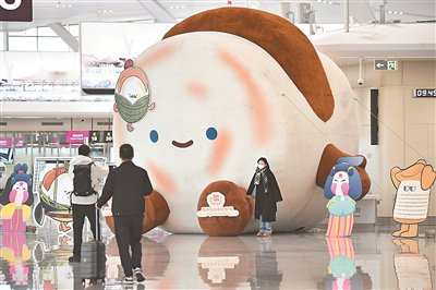 陝西西安鹹陽國際機場T5航站樓出發大廳內,乘客與肉夾饃造型的吉祥物合照。新華社記者 邵瑞攝