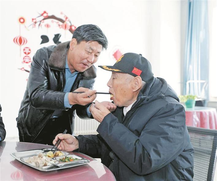 祁善海（左）给五师八十一团怡心养老院送去慰问品，并陪老人吃饺子（资料图片）。周莉 摄