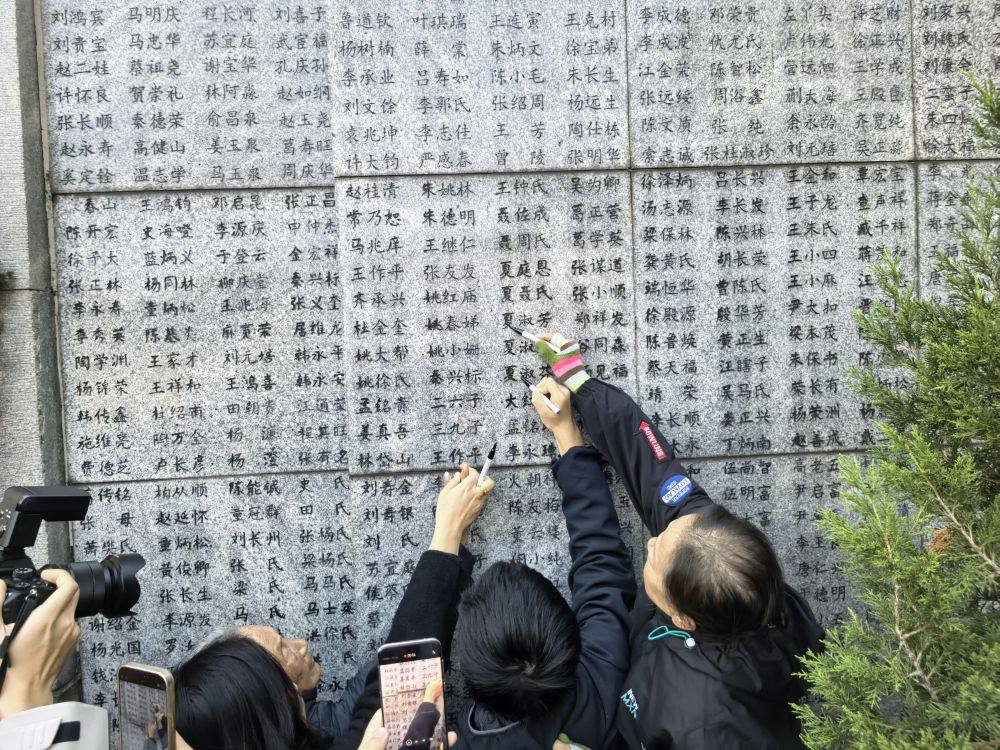 南京大屠殺倖存者夏淑琴指著「哭牆」上親人的名字，女兒和曾外孫替她為親人的名字「描新」。新華社記者邱冰清攝