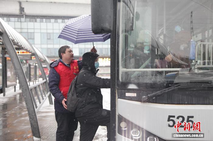 武漢公交六公司「24小時應急先鋒隊」成員李德龍在武漢站公交站台冒雪為乘客撐傘。塗舉學 攝