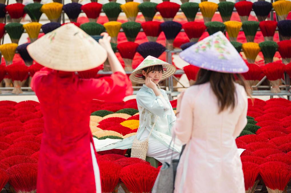 3月24日，在越南广富桥村，游客在晾晒的香签旁拍照。新华社记者朱炜摄