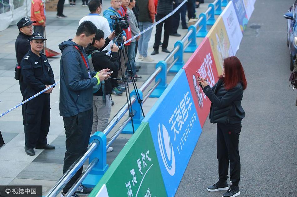 镜头拉远,冬日娜和杜锋并肩站在赛道旁的护栏边,周围是攒动的人头和飘扬的旗帜。完成扫码的两人似乎正进行着简短的交流,身后巨大的赛事背景板无声地宣告着这场亚洲田径盛事的主场。