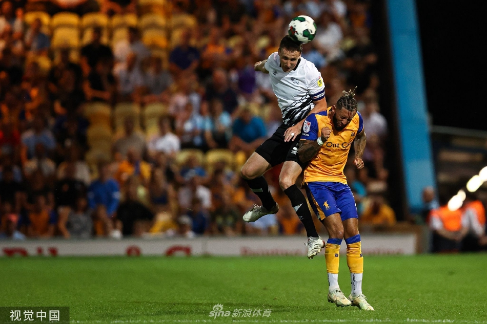 曼斯菲特球员突破重围后振臂怒吼庆祝进球，面容因激情而扭曲，身后是沮丧的对方后卫和远方看台上陷入疯狂的主队球迷海洋