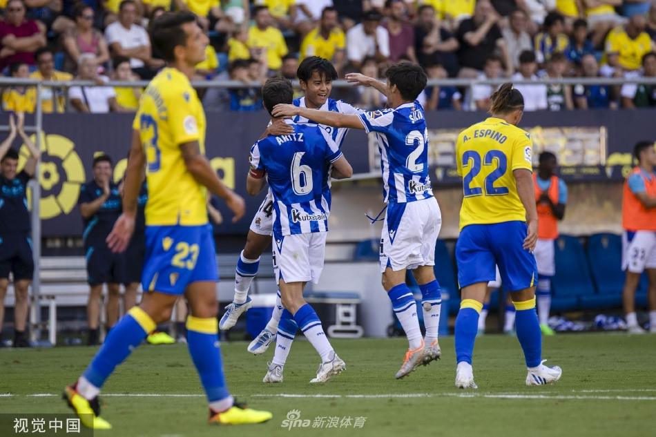 皇家社会球员在破门瞬间激动地奔向角旗区庆祝，身后是垂头丧气的加的斯后卫。